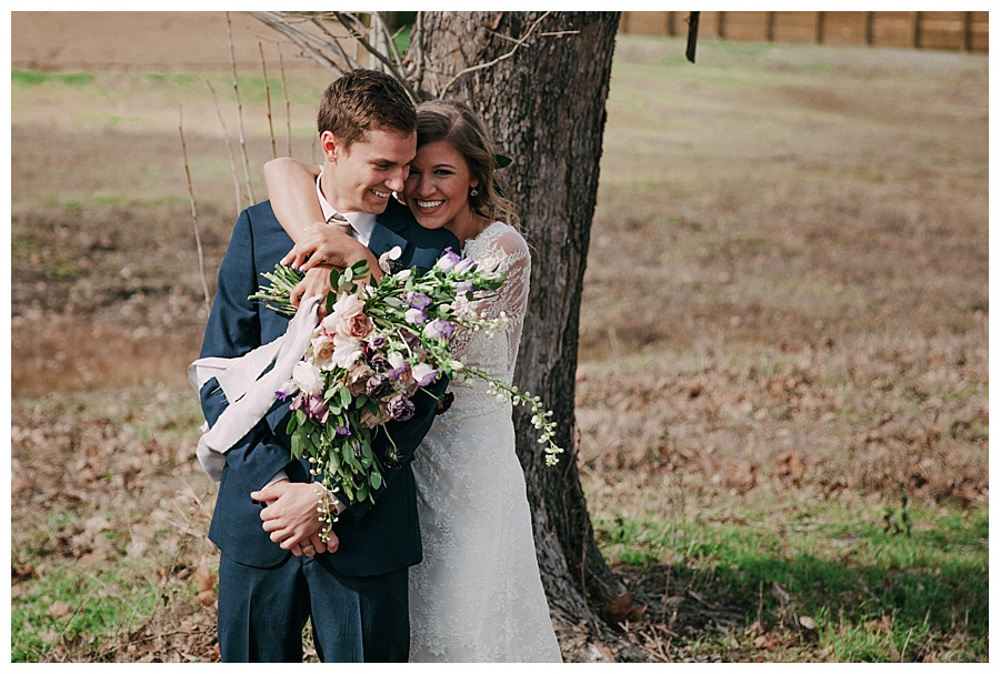 First Wedding at The Farmhouse Bride hugging groom from behind in front of tree